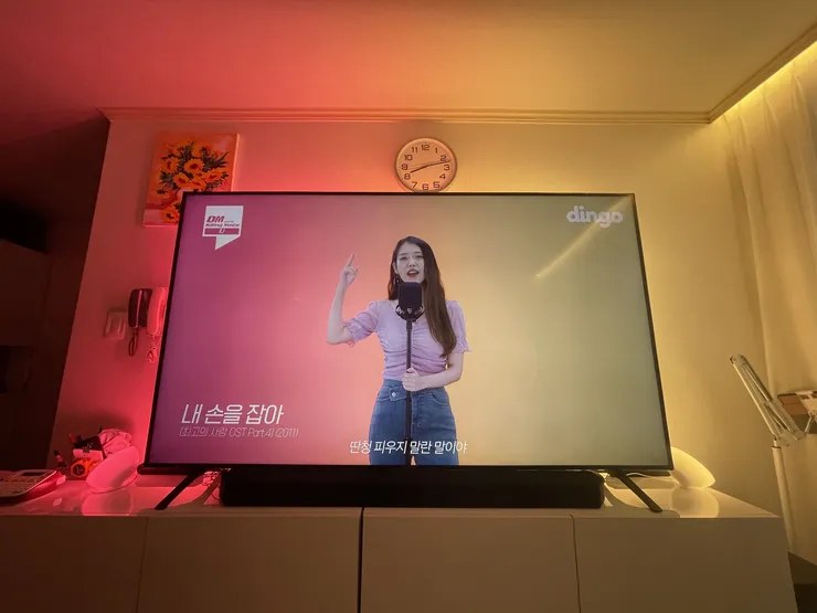 필립스 휴 TV 연동 조명이 켜진 거실: TV 화면의 분홍·노랑 색에 맞춰 벽과 커튼, TV 아래 조명이 같은 색으로 물든 모습