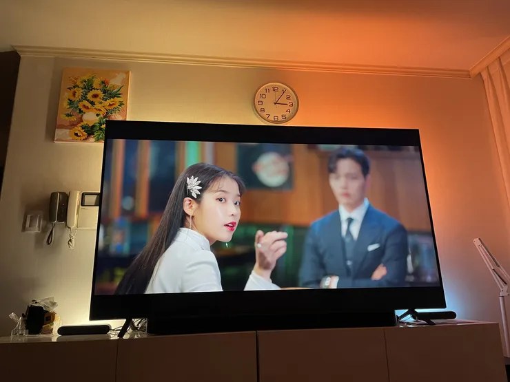 필립스 휴 TV 연동 중인 거실: 따뜻한 장면에 맞춰 TV 뒤 벽과 천장이 주황빛으로 물든 모습